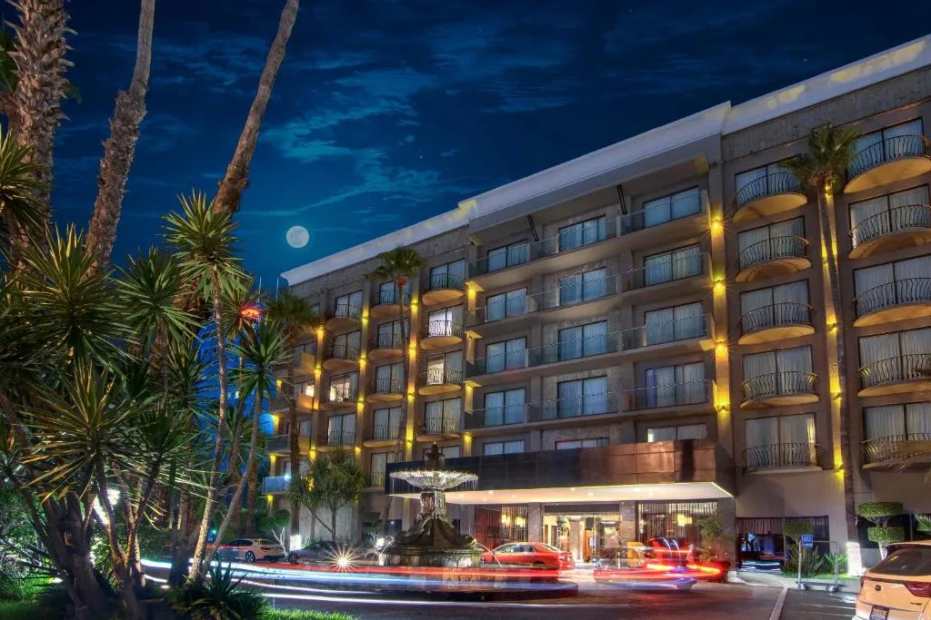 Night exterior of Hotel Lucerna Tijuana with fountain and palm trees