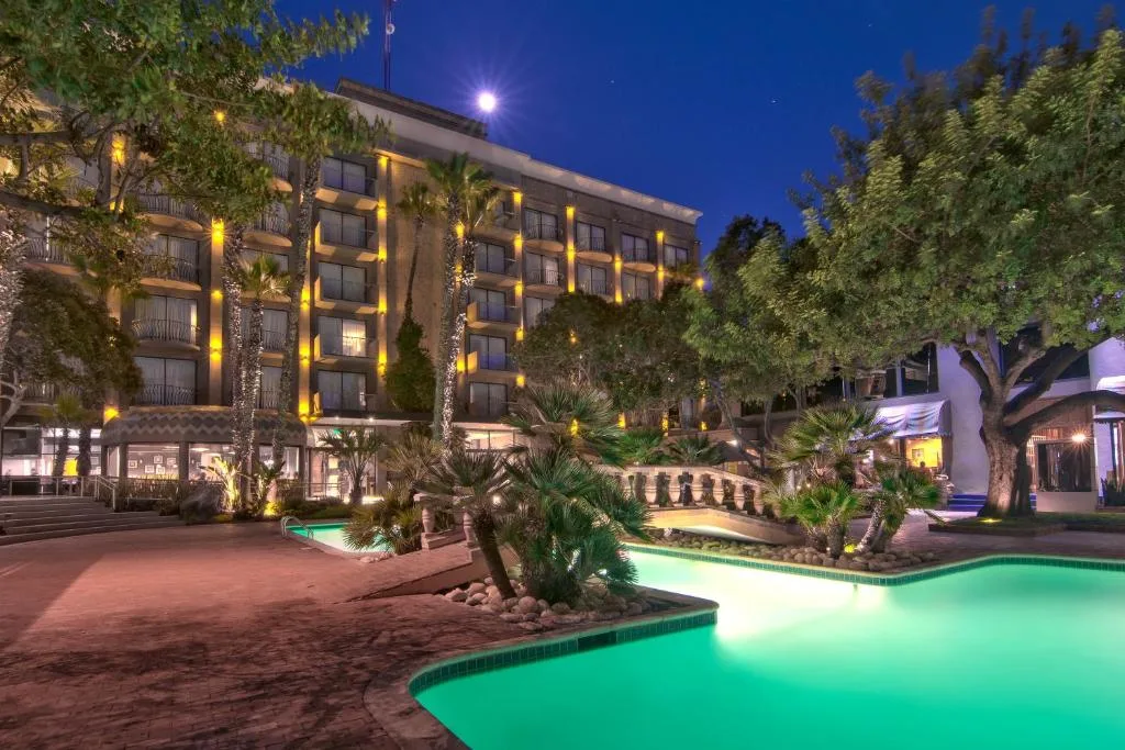 Hotel Lucerna Tijuana pool at dusk with palm trees and the lit hotel facade