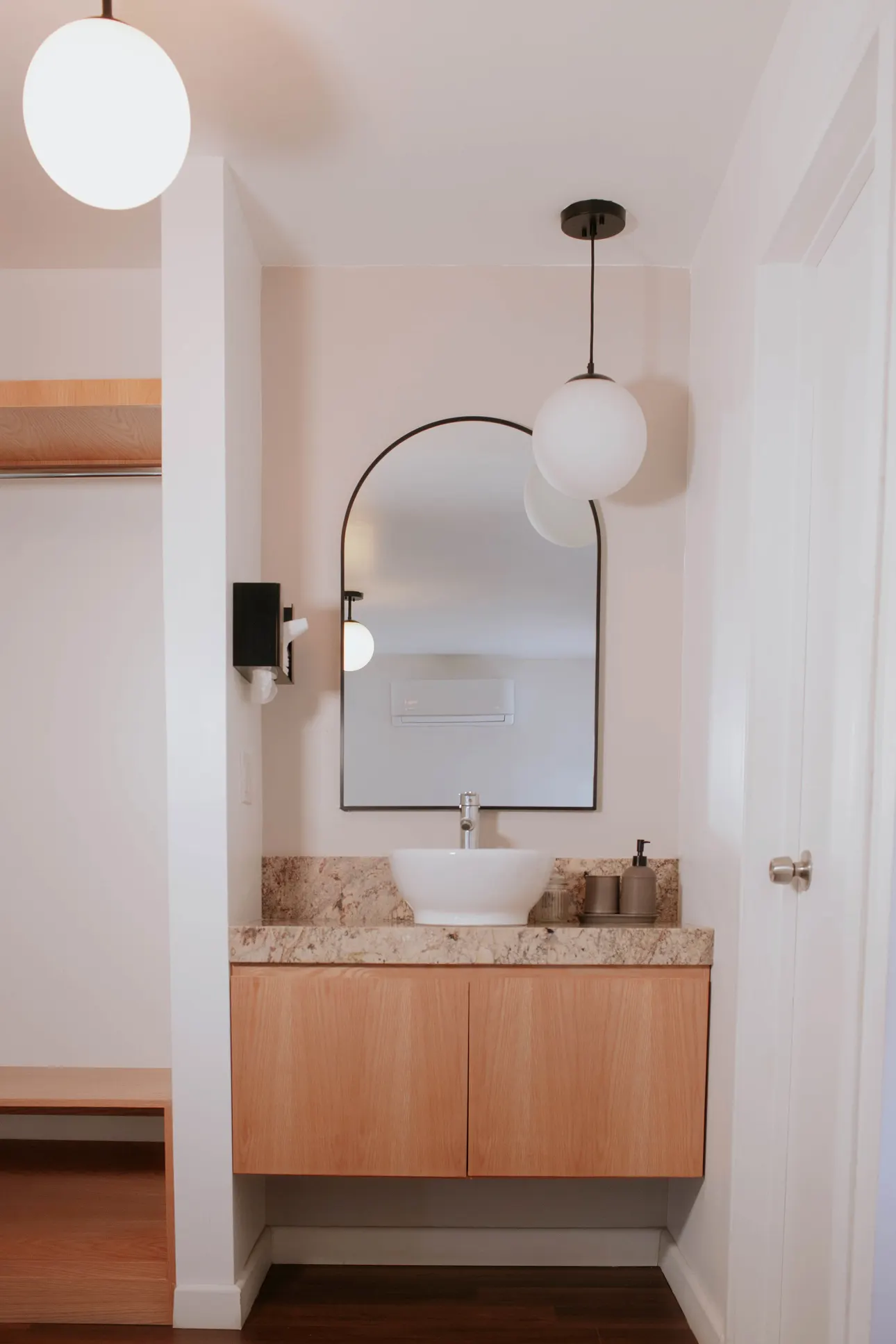Bathroom vanity with stone countertop, arched mirror and soft pendant lighting